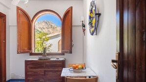 A narrow hallway with a wooden cabinet, a table with fruit, and a view through a window with open shutters. - Domus Sicily - Il nido di suerte sea view (Palermo)