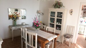 Un'area pranzo con un tavolo in legno, sedie bianche, un mobiletto con vetrate e un lampadario.