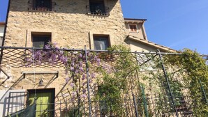 Un edificio in pietra con un balcone, una porta verde e edera fiorita di colore viola.