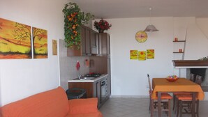 Una sala de estar con un sofá, una mesa de comedor con sillas, una zona de cocina con armarios y una estufa, y una chimenea.