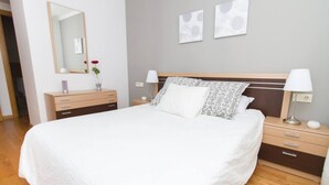 Un dormitorio ordenado con una cama grande, un aparador, mesitas de noche y un espejo.