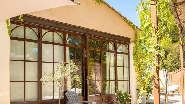 A building with large arched windows, a patio with a chair and table, and potted plants. - Bed & Breakfast in a Farmhouse- air conditionned - Lacoste (Lacoste)