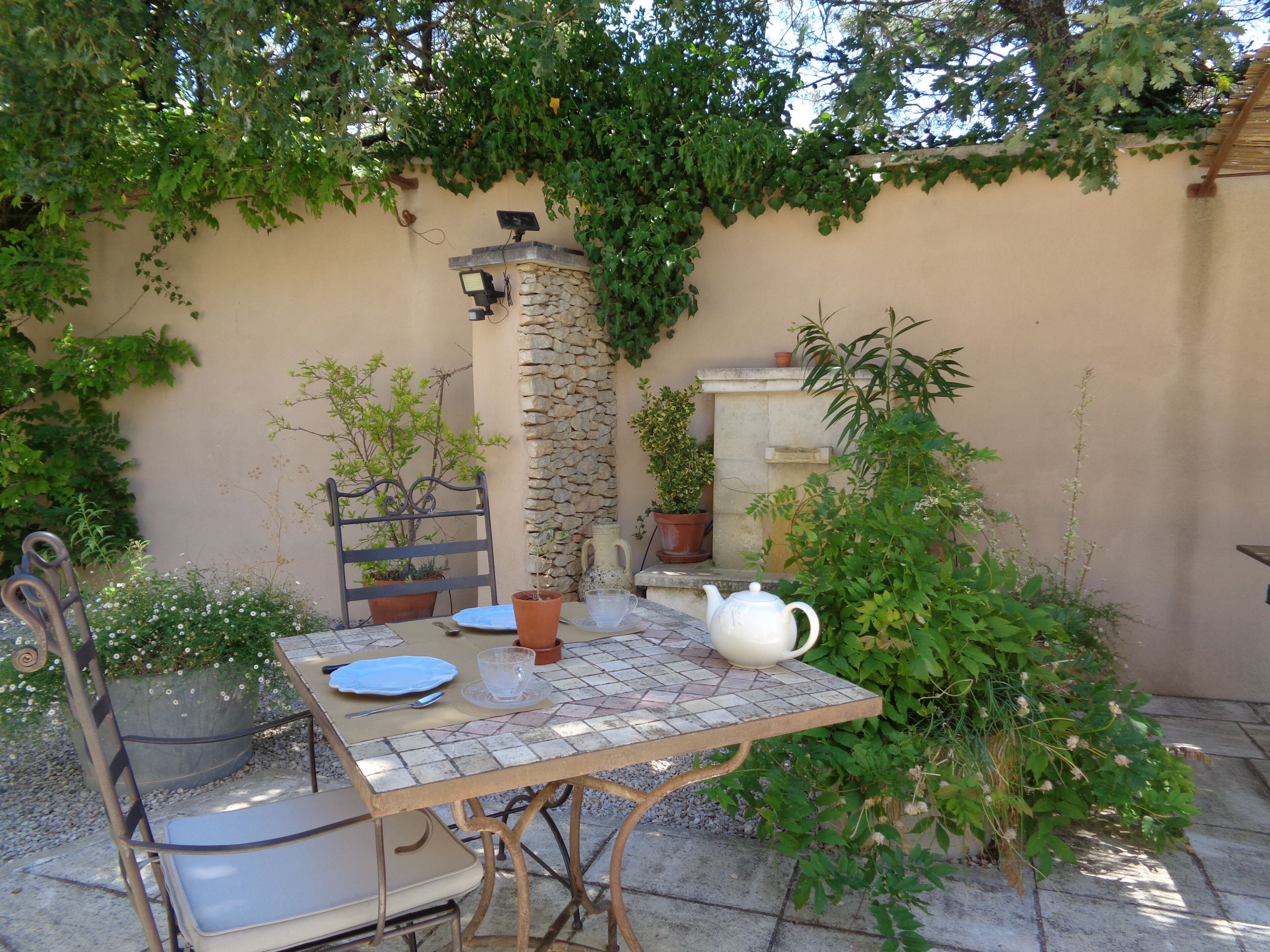 A patio with a table, chairs, a stone wall, and potted plants.