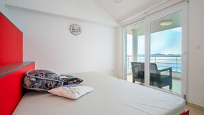 A modern bedroom with a bed, a red bench, a patterned pillow, and a view of the sea through a sliding glass door. - Stunning private villa for 12 guests with hot tub, private pool, WIFI, A/C, TV and patio (Zadar)