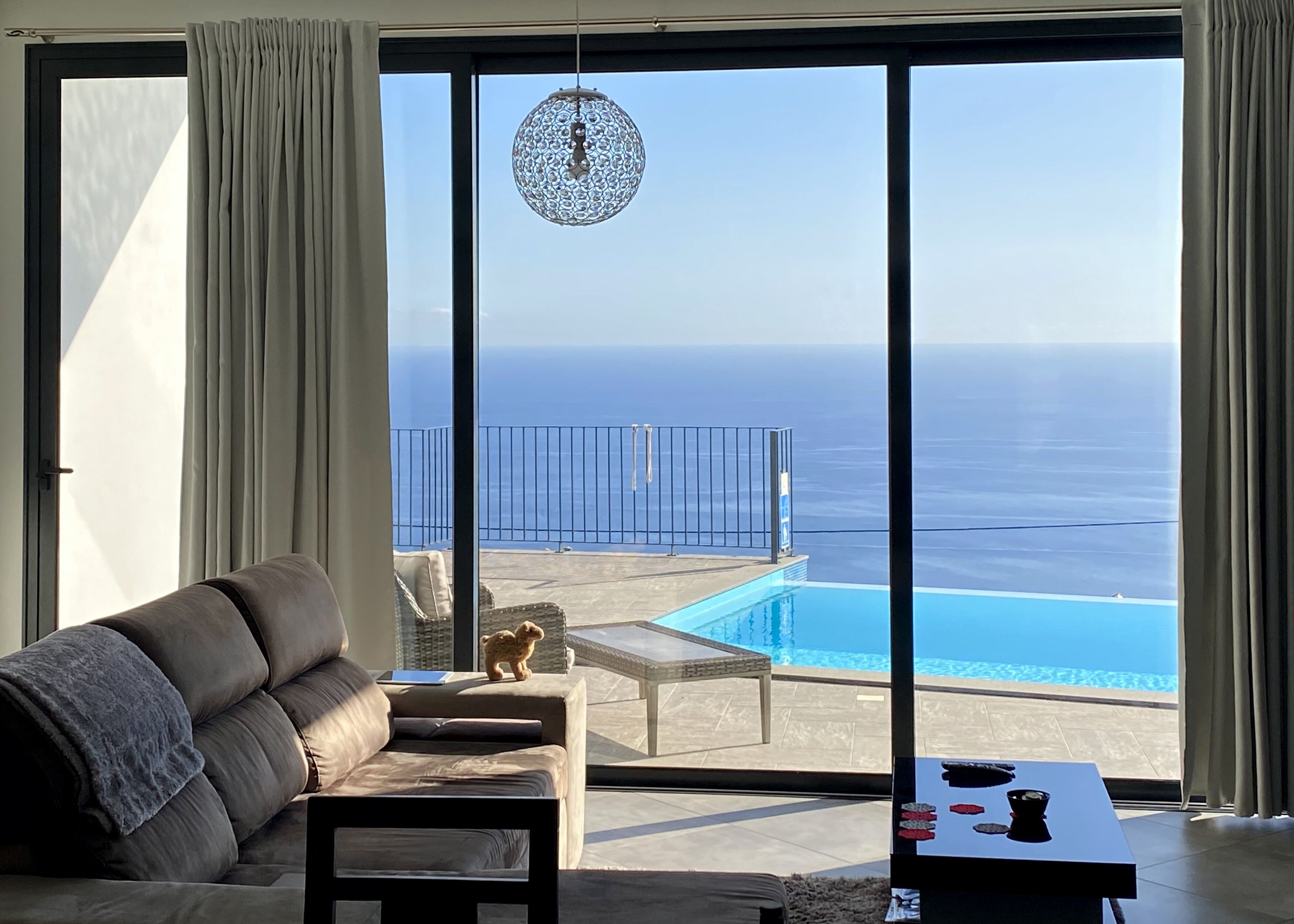 A modern living room with a sofa, a small table, and a view of a pool and ocean.