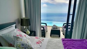 A hotel room with a bed, a nightstand, a lamp, a view of the ocean, and a balcony with chairs and a table. - Syso House - Extraordinary ocean view ----- (New Promotions) ----- (Arco da Calheta)