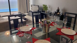 A dining area with a glass table set for four, a bottle of wine, and a view of the ocean through large windows. - Syso House - Extraordinary ocean view ----- (New Promotions) ----- (Arco da Calheta)