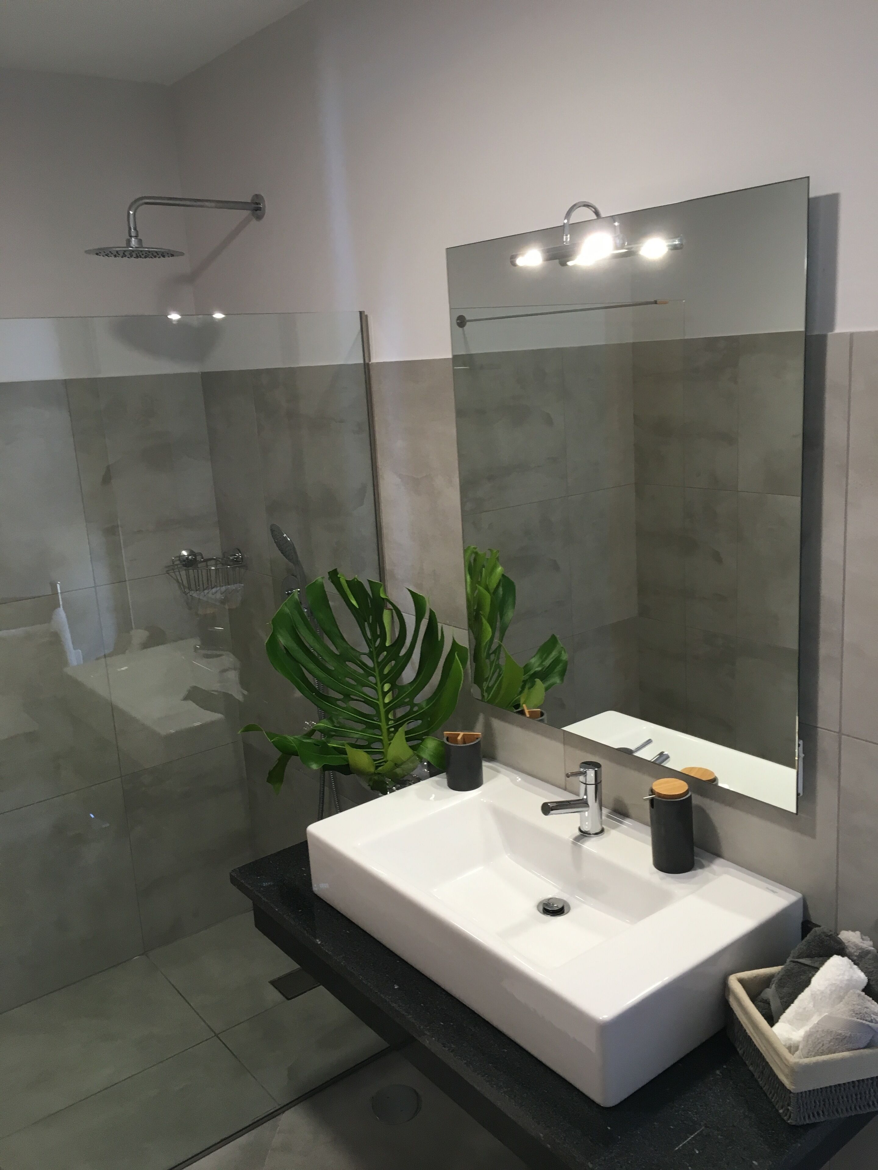 Een moderne badkamer met een grote spiegel, een wit wastafelmeubel en een douchehoek.