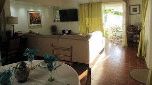 Un salon comprenant un canapé, un téléviseur fixé au mur et un coin repas avec une table dressée pour deux personnes.