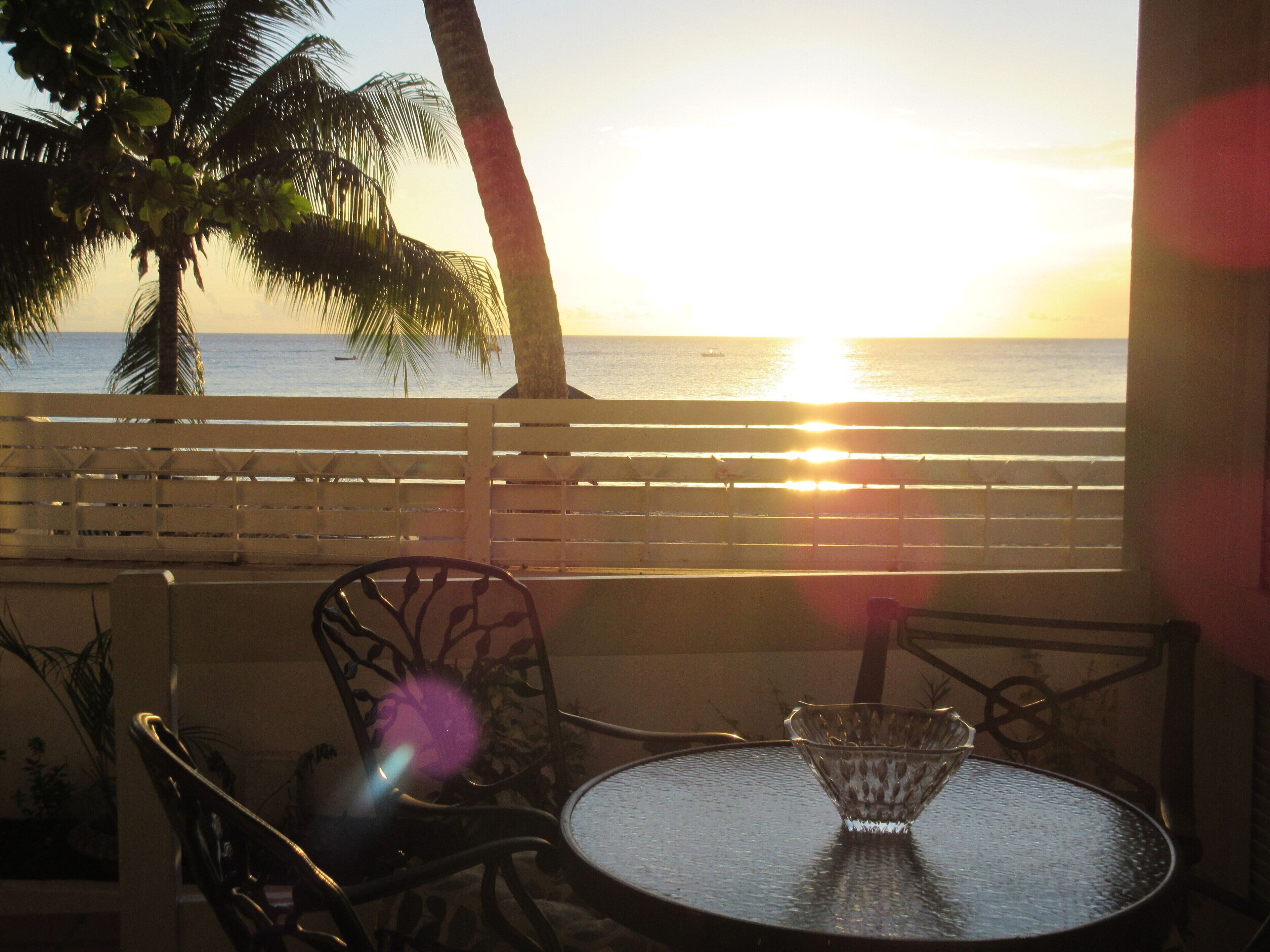 A table with a glass bowl, chairs, and a view of the sunset over the ocean.