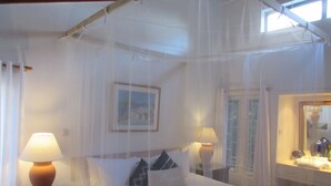Une chambre à coucher avec un lit à baldaquin, des lampes de chevet, un tableau encadré au mur et une fenêtre avec des rideaux.
