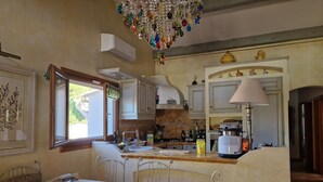 A kitchen with a dining area, featuring a glass table, chairs, a chandelier, and various kitchen appliances. - Single-storey house, rated 4*, air-conditioned, private pool. 10 minutes from the sea. (La Colle-Sur-Loup)