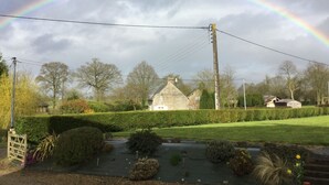 Paisagem rural com uma casa de pedra, um arco-íris e um jardim bem cuidado.