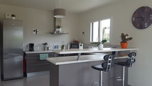 A modern kitchen with a refrigerator, microwave, and coffee maker. There are two bar stools and a large clock on the wall. - New holiday house 100 meters from the sea (Kerlouan)