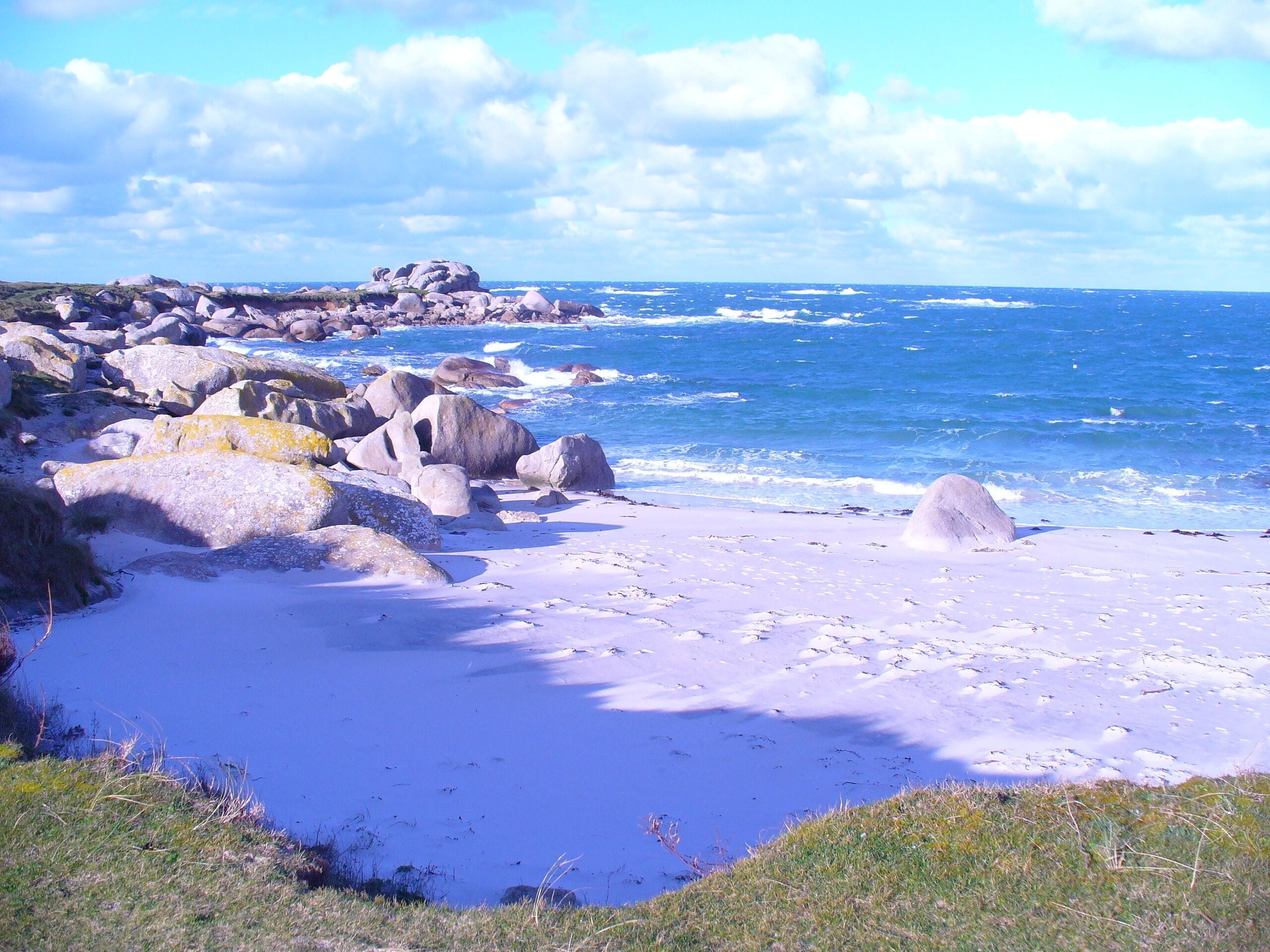 Une plage rocheuse parsemée de gros blocs et offrant une vue dégagée sur l’océan.