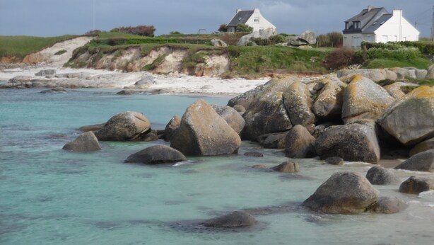 A coastal scene with large rocks in the foreground and houses on a grassy hill in the background. - New holiday house 100 meters from the sea (Kerlouan)