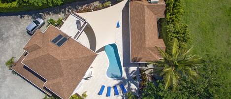 An aerial view of a property with a swimming pool, a covered patio, and a car parked in the driveway.