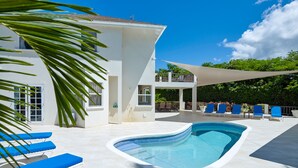 A modern pool area with blue lounge chairs, a clear blue pool, and a white building with a balcony. - Luxury 6 Bed Villa With Pool, Mullins Bay (Mullins)