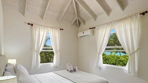 A bedroom with a bed, two windows with curtains, an air conditioning unit, and a view of greenery outside. - Luxury 6 Bed Villa With Pool, Mullins Bay (Mullins)