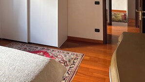 A room with a wooden ceiling, a white wardrobe, a hanging light fixture, a patterned rug, and a door leading to another room.