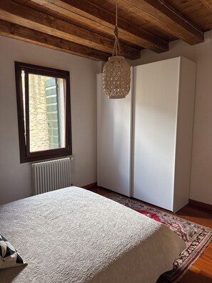 A bedroom with a bed, a window, a radiator, a wardrobe, and a hanging light fixture.