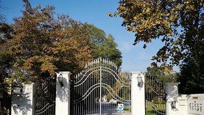 A gated entrance with a metal gate and white pillars, surrounded by trees with autumn leaves.