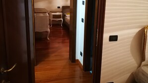 A hallway with wooden flooring leading to a room with a bed and a nightstand.