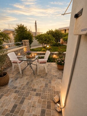 An outdoor patio with a table and chairs, stone flooring, potted plants, and a view of a building with a statue.