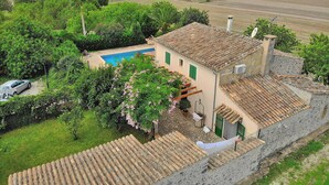 A villa with a swimming pool, surrounded by lush greenery and agricultural fields.