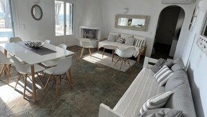 A spacious living area with a stone floor, white furniture, and a fireplace. - Villa Meraki (Agkeria)