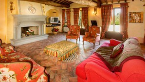 Una sala de estar tradicional con chimenea, sillones con estampado floral, un sofá rojo y un televisor sobre un mueble.