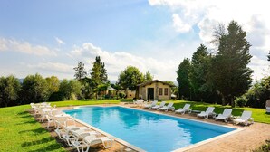 Una piscina rectangular con un bordeado de azulejos, rodeada de sillas y mesas de descanso blancas.