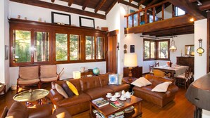 A spacious living area with a high ceiling, wooden beams, a dining area, and large windows.