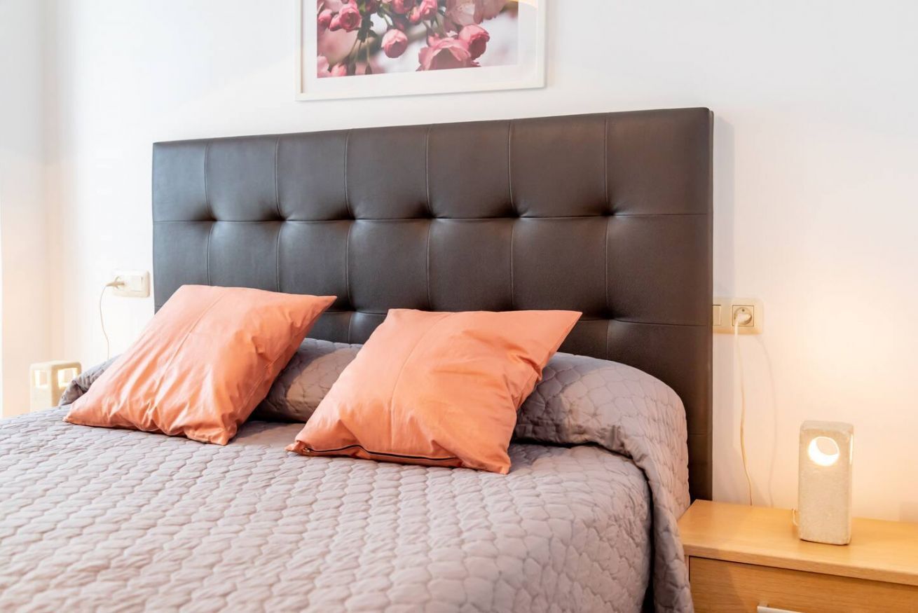 En pænt redt seng med mørkt sengegavl, to puder og et natbord med en lampe.