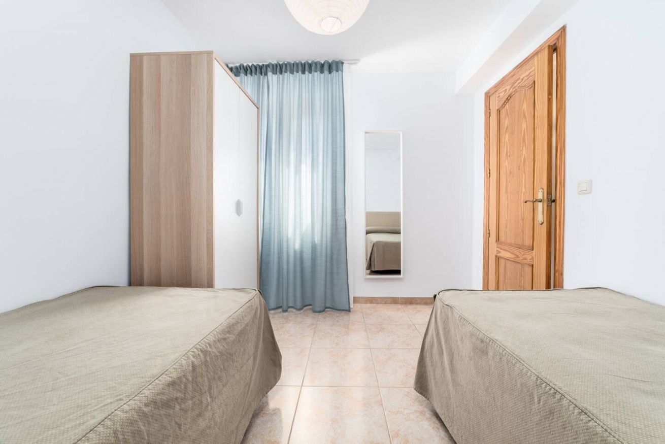 A room with two beds, a wooden wardrobe, a mirror, and a door.