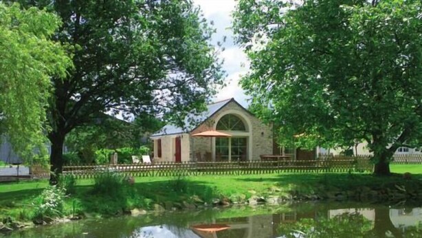 A stone building with a red roof, surrounded by lush greenery and a pond with flowers. - Au Bas Chalonge Gite in Ligné (Ligné)