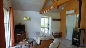 A living room with a sofa, a television on a wooden cabinet, a fireplace, and a window with curtains. - Au Bas Chalonge Gite in Ligné (Ligné)