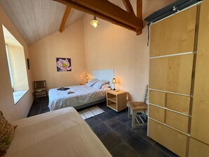Un dormitorio con una cama, mesitas de noche, una silla, un armario de madera, un cuadro y una ventana.