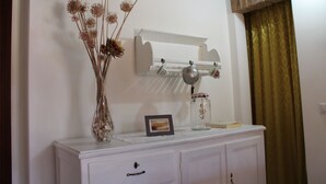 Une commode blanche avec un miroir, un vase contenant des fleurs séchées et un petit tableau encadré.