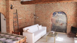 Une pièce avec un canapé blanc, une table basse en verre, un mur en briques orné d’une fresque et une poutre en bois au plafond.