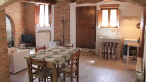Une cuisine rustique avec un mur en briques, des poutres en bois, une table à manger avec des chaises, un téléviseur et un petit réfrigérateur.