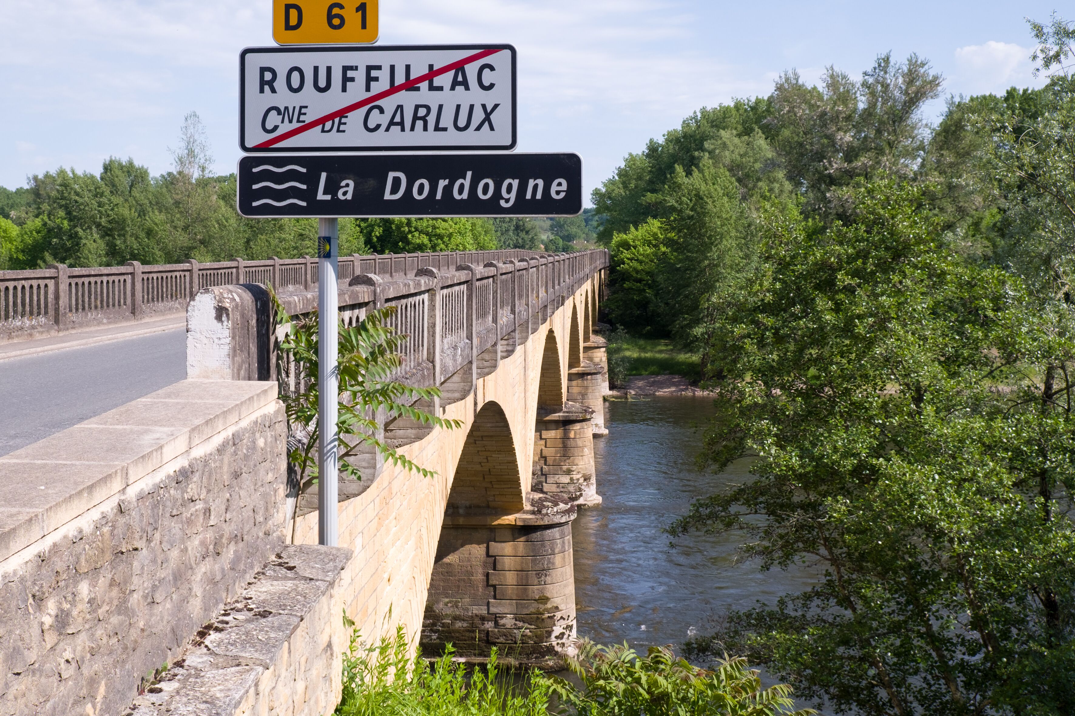 A stone bridge over a river with signs indicating directions to Rouffillac and La Dordogne.