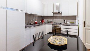 Una cocina compacta con armarios blancos, estufa a gas, pileta y una pequeña mesa de comedor con sillas.