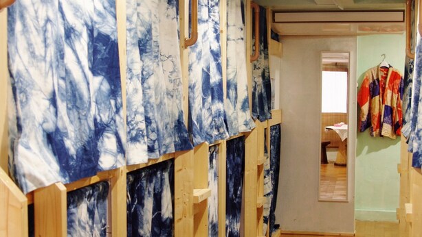 A hallway with wooden shelves displaying artwork, a wooden floor, and a door leading to another room. - Kichinan - Hostel (Osaka)
