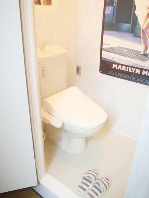 A small, white bathroom with a toilet, a wall-mounted sink, and a poster of Marilyn Monroe. - Kichinan - Hostel (Osaka)