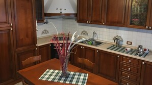 A kitchen with wooden cabinets, a dining table with chairs, a vase with plants, and a checkered placemat.