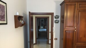 A hallway with a wooden door leading to a room, a wall-mounted telephone, and a shelf with decorative items.