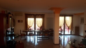 A spacious living room with a dining area, large windows with curtains, a staircase, and a kitchen area.