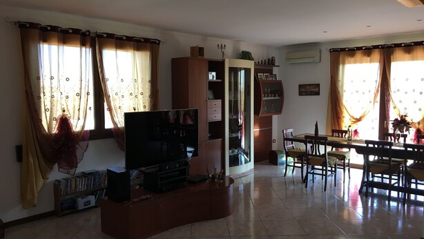 A living room with a TV, bookshelves, a dining area with chairs, and curtains.