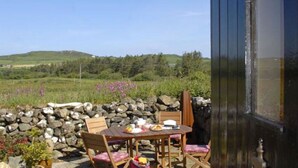 A rustic outdoor dining area with a stone wall, wooden table, and chairs. - Escape To This Hidden Gem & Relax In Tranquility - Beaches & Coastal Path Nearby (st nicholas)